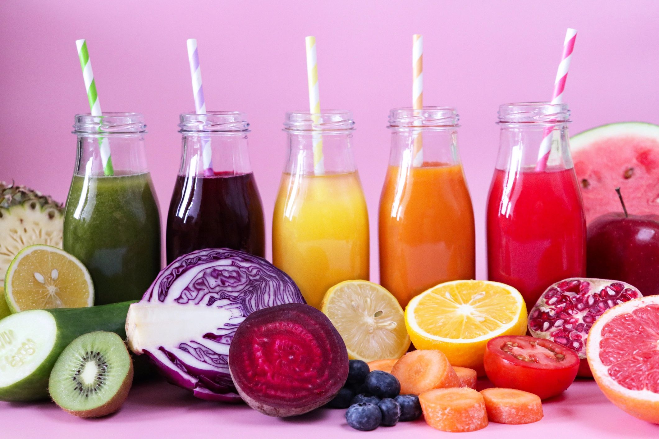 Botellas de jugos de frutas de colores sobre fondo rosado